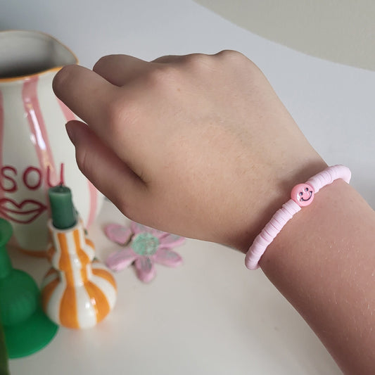 A light pink clay bracelet with smiley charm